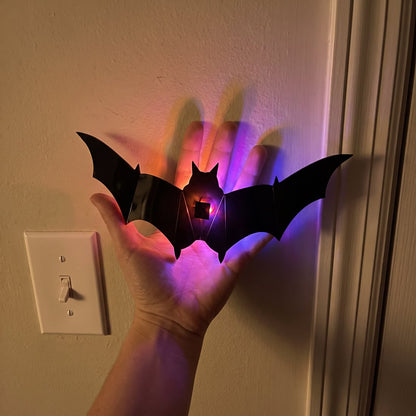 A bat held in a hand beside a light switch for scale